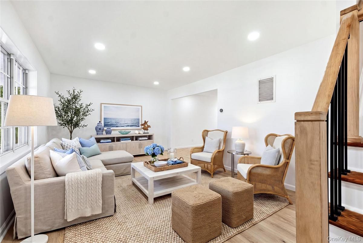 Bright living area featuring wood-finish flooring, recessed lighting, and a prominent staircase with wood handrail and black balusters