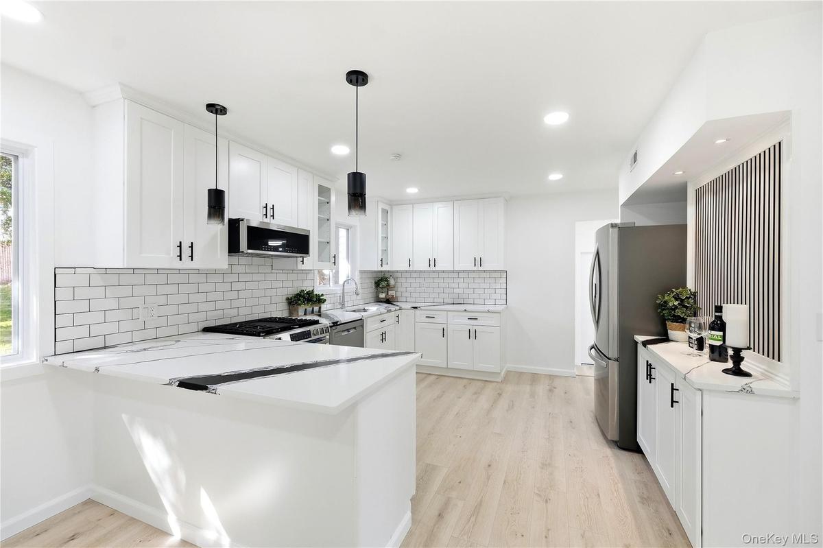 White shaker cabinetry with matte black hardware, white subway tile backsplash, stainless steel appliances, and wood-finish flooring