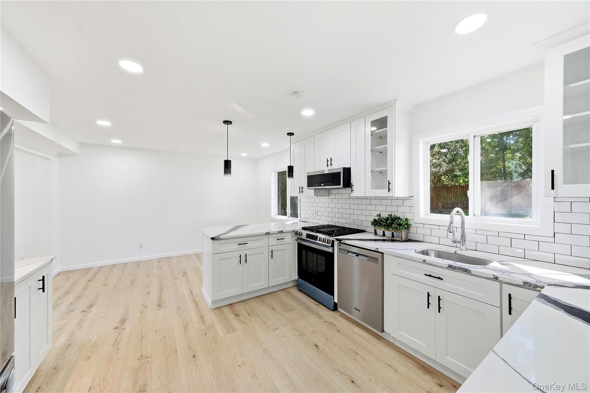 Modern kitchen featuring light wood-finish flooring, white shaker cabinetry, stainless steel appliances, a subway tile backsplash and dining area