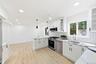 Modern kitchen featuring light wood-finish flooring, white shaker cabinetry, stainless steel appliances, a subway tile backsplash and dining area