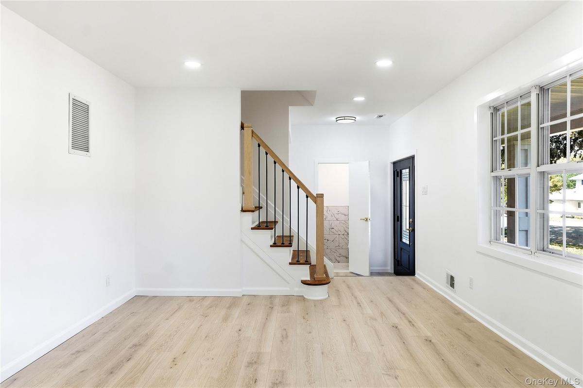 Light wood-finish flooring, white walls, recessed ceiling lighting, and a staircase with wood risers and a black metal railing