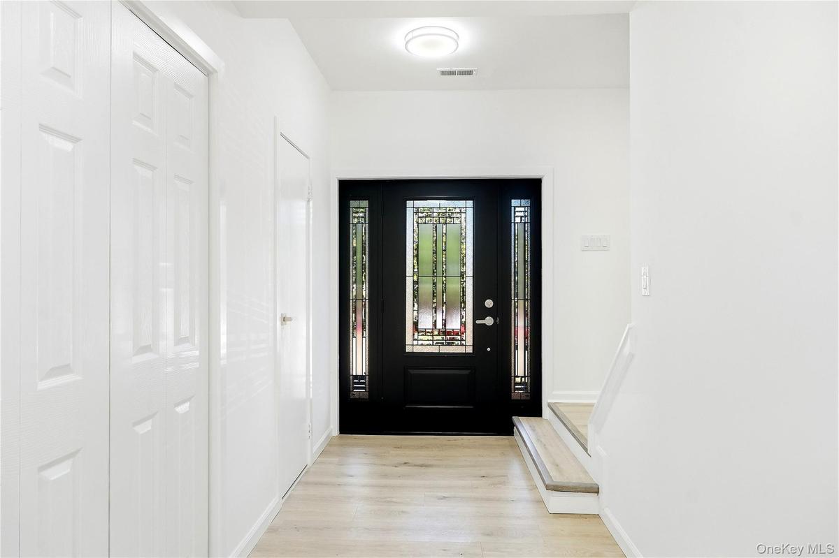Black entry door with decorative glass side panels, wood-finish flooring, two white paneled closet doors, and a half bathroom
