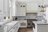 White cabinetry with gold-tone hardware, marble countertops and backsplash, stainless steel range, built-in microwave, and wood floors.