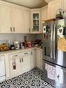 White cabinetry with crown molding, glass-front corner cabinet, stainless steel refrigerator, patterned floor tile, and light-toned countertops