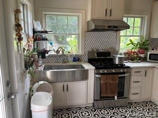 Stainless steel range, stainless steel farmhouse sink, diamond-patterned backsplash, light-toned cabinetry, and patterned floor tile