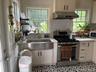 Stainless steel range, stainless steel farmhouse sink, diamond-patterned backsplash, light-toned cabinetry, and patterned floor tile