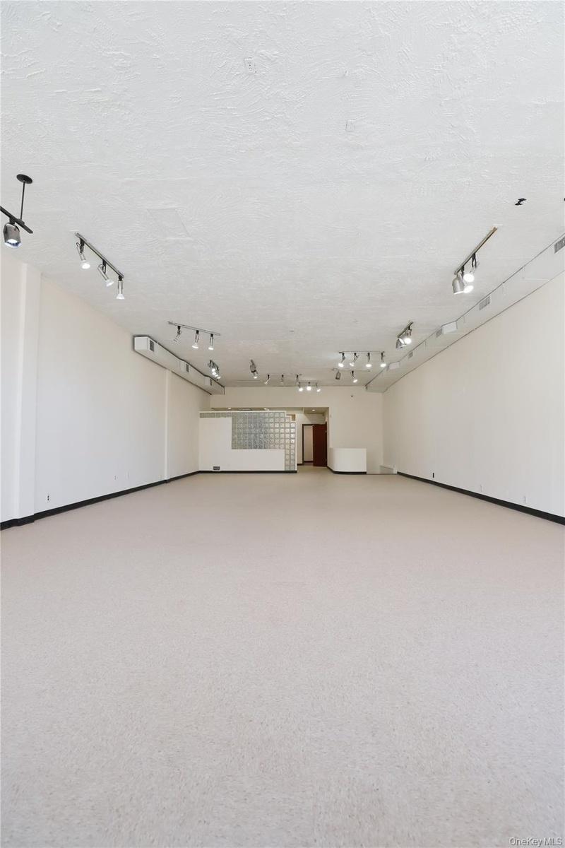 Expansive open-concept room with light-colored flooring, white walls, and track lighting fixtures