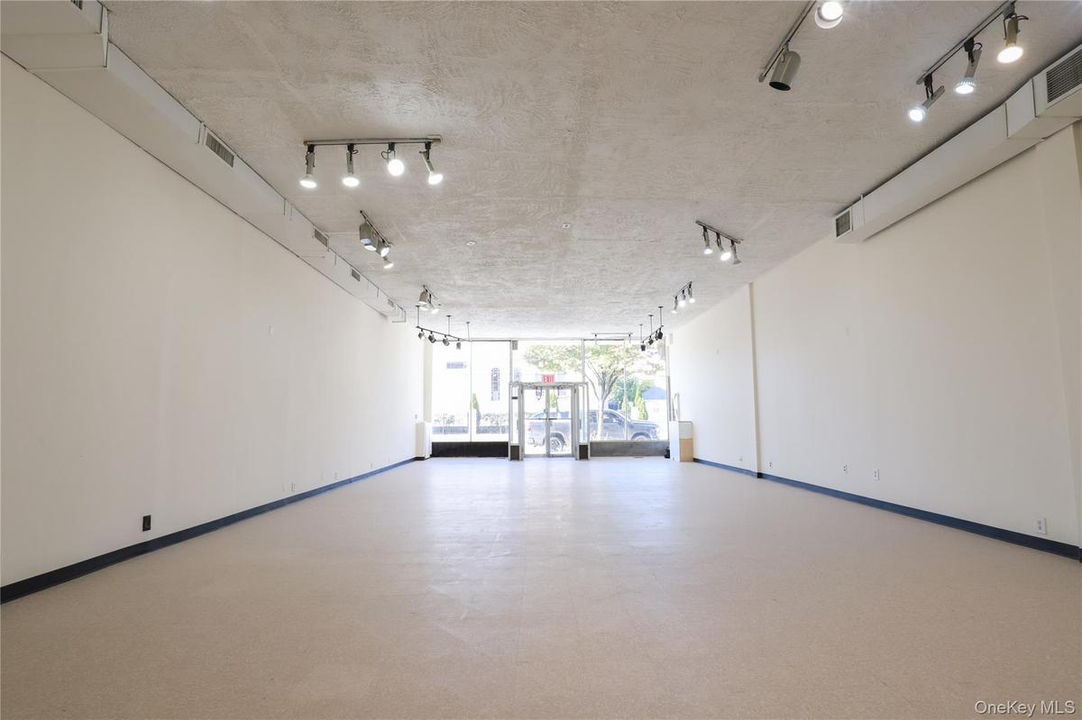 Expansive open-concept room with light-colored flooring, white walls, and track lighting fixtures