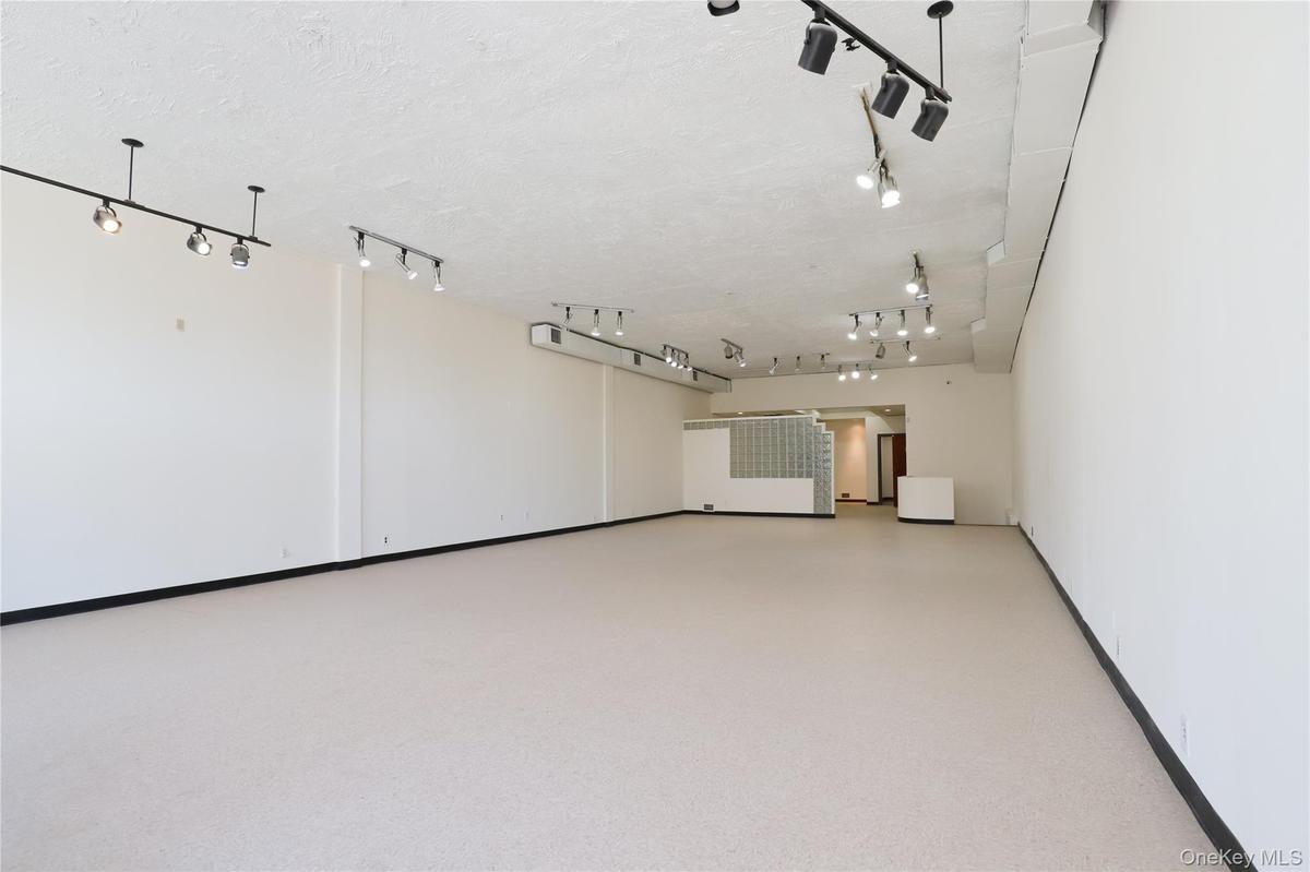 Spacious open-concept interior featuring light-colored flooring, extensive track lighting, and white walls