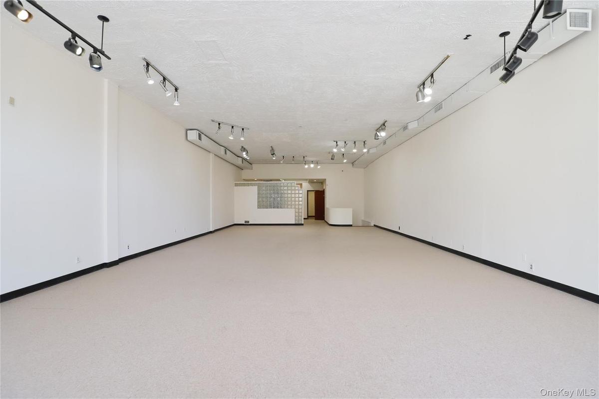 Expansive open-concept room with light-colored flooring, white walls, and track lighting fixtures