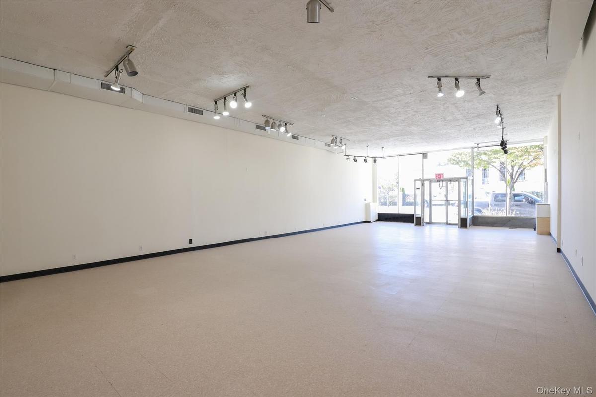 Expansive open-concept room with light-colored flooring, white walls, and track lighting fixtures