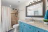 The updated second bath features a turquoise vanity with granite countertop, framed mirror, modern lighting, and a tiled walk-in shower with built-in 