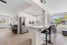 The updated kitchen (2025) pairs crisp white cabinetry and stainless steel appliances with expansive counter space and a wraparound breakfast bar that