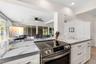 The updated kitchen (2025) showcases dramatic stone-look countertops, white Shaker-style cabinetry, stainless steel appliances, recessed lighting, and