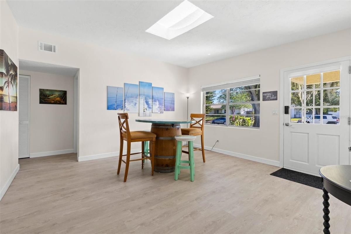Step inside to a bright, open dining area with 2025 luxury vinyl plank flooring, a skylight overhead, and broad front windows that fill the space with