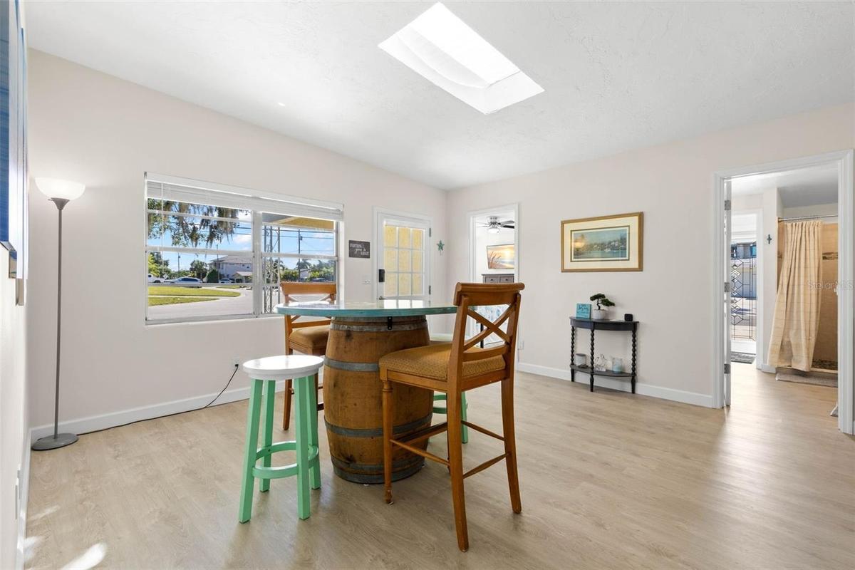 The bright dining area features 2025 luxury vinyl plank flooring, a skylight overhead, broad front windows, and plenty of room for everyday meals or e