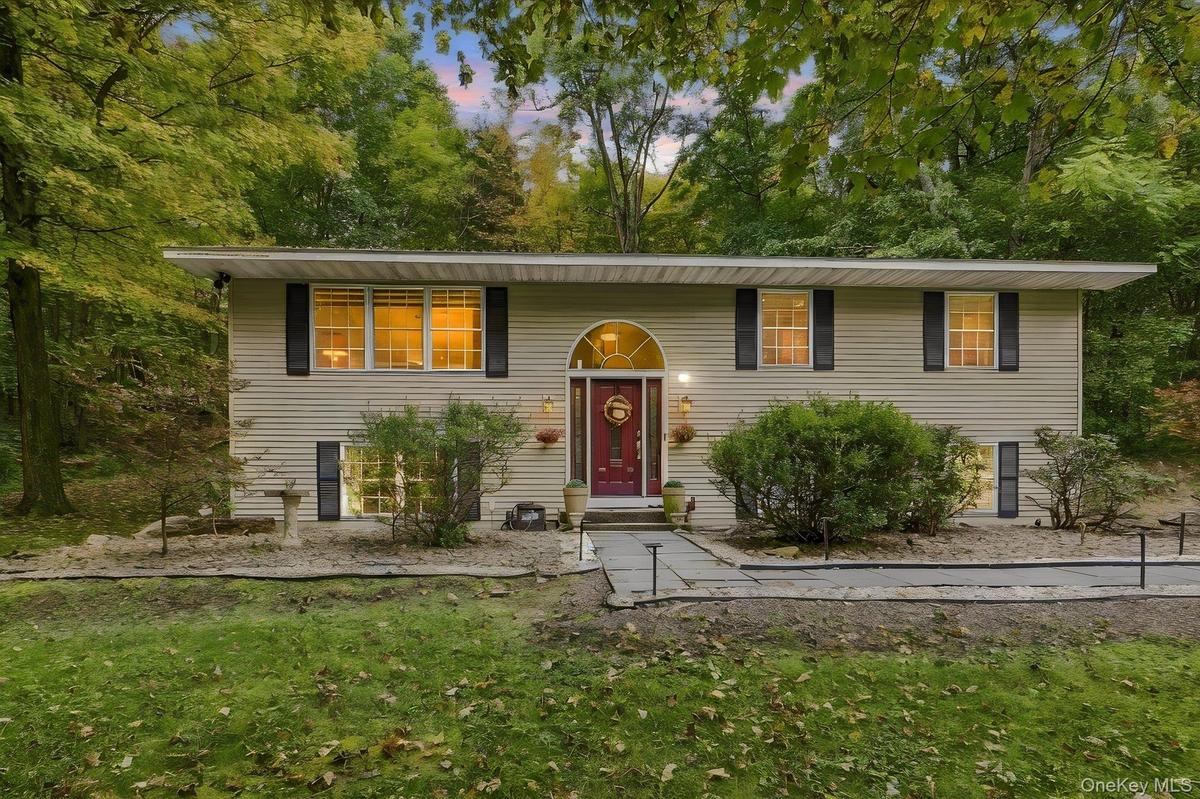 Bi-level residence featuring light-toned siding, a vibrant red entry door with an arched transom, and black window shutters