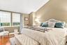 Hardwood flooring, two windows with Roman shades, upholstered headboard, pitched ceiling, and neutral wall tones