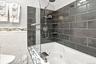Bathtub with a glass shower panel, dark subway tile surround, integrated shelving, and a rain showerhead