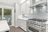 Stainless steel range with a ventilation hood, white cabinetry, tile backsplash, and light-toned countertops