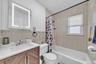Illuminated vanity mirror, wood-finish vanity with an integrated sink, full bathtub with a shower fixture, and tiled walls