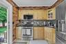 Kitchen featuring light wood cabinetry, a mosaic tile backsplash, black countertops, stainless steel appliances, and brick-patterned wall accents