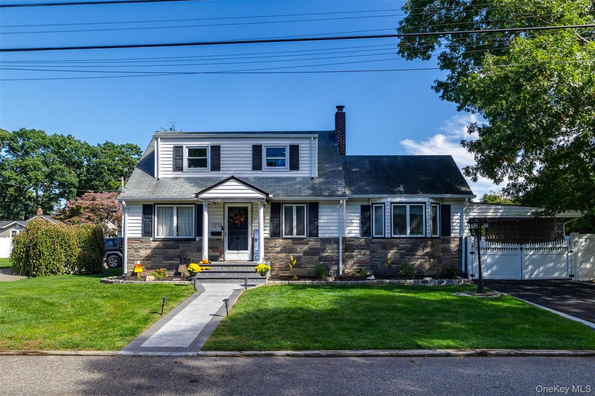 Cape Cod style residence featuring a stone and siding facade, a paved driveway, and a front walkway with integrated lighting