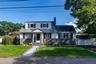 Cape Cod style residence featuring a stone and siding facade, a paved driveway, and a front walkway with integrated lighting