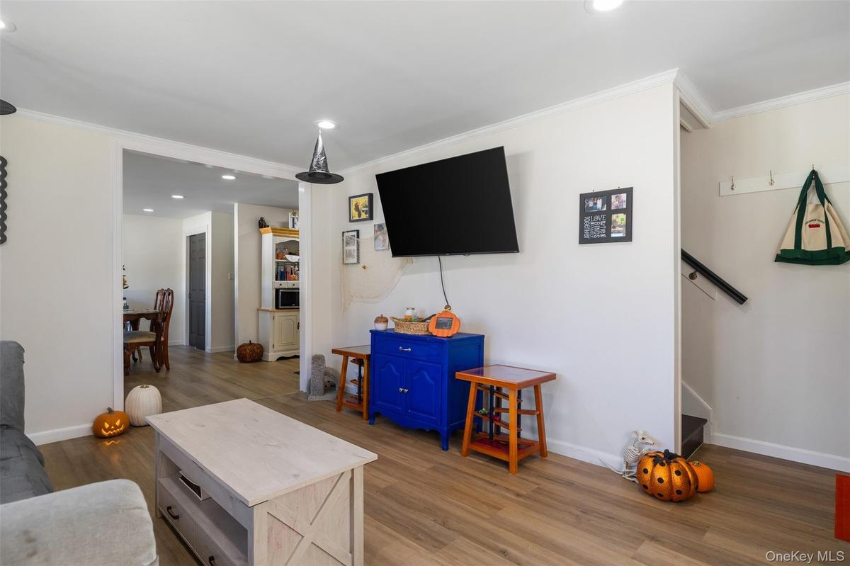 Wood-finish flooring throughout, recessed ceiling lighting, crown molding, and an open entryway to an additional room