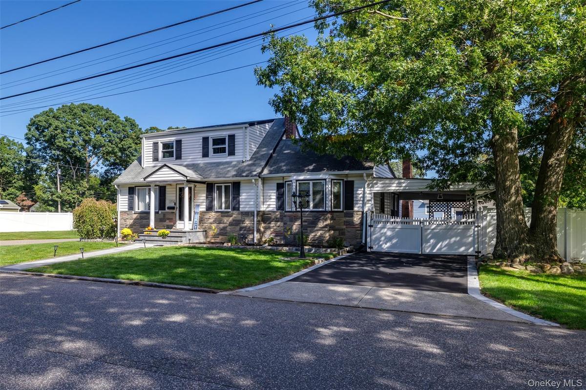 Traditional-style residence featuring a stone-clad facade, a covered entry, a paved driveway, and mature landscaping