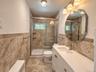 Tiled flooring and wainscoting, glass-enclosed shower with window, white vanity with integrated sink, contemporary vanity lighting, and decorative mir