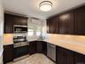 Dark wood-finish cabinetry with crown molding, stainless steel appliances, white subway tile backsplash, light-toned countertops, and a flush mount ce