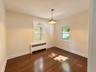 Warm wood-finish flooring, two large windows, a radiator unit, a bronze-finish pendant light fixture, and crown molding