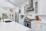Bright kitchen featuring white cabinetry, stainless steel appliances, a herringbone tile backsplash, an undermount sink with a brass-finish faucet, an