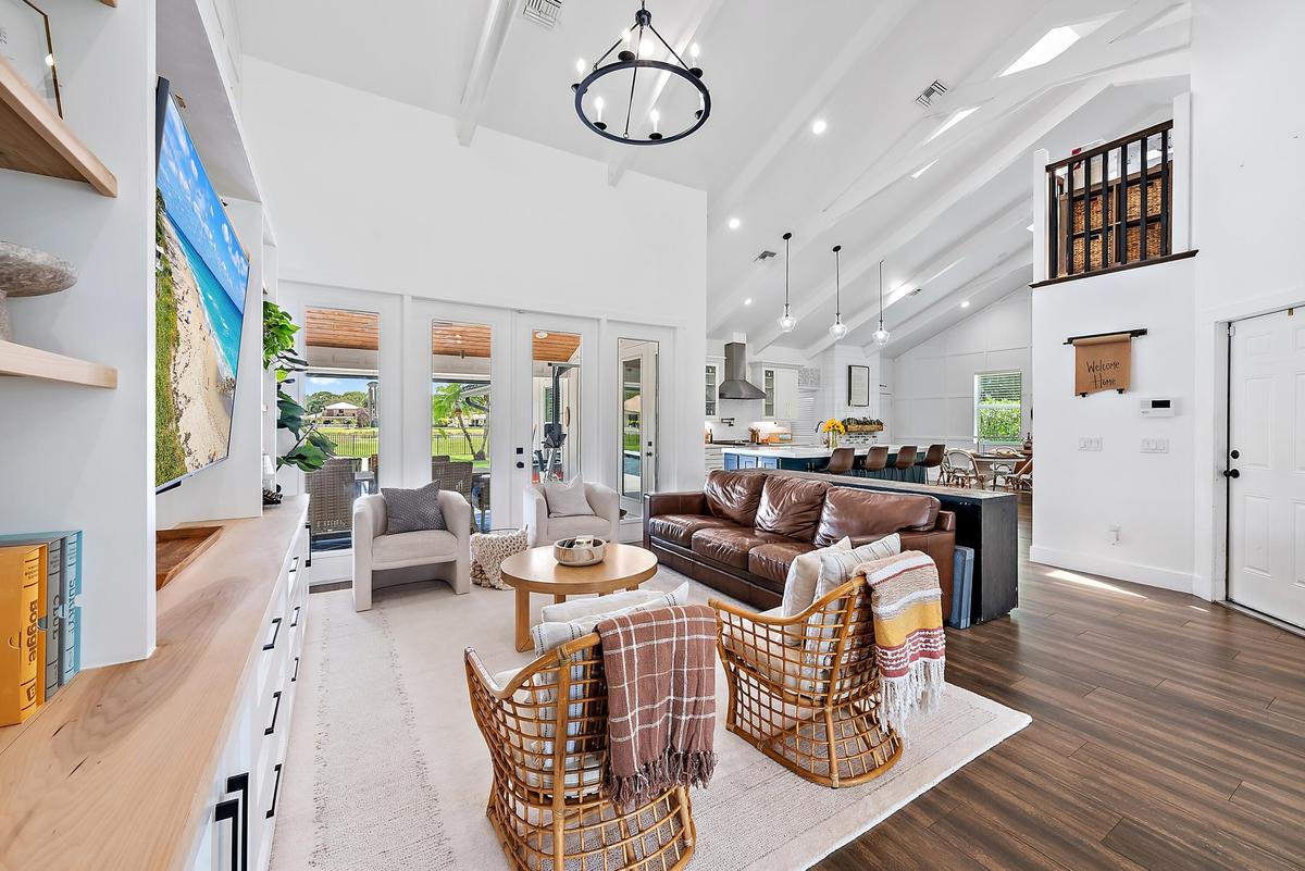 Vaulted white ceilings with exposed beams, wood-look tile flooring, built-in media console with shelving, white French doors, and an upper-level inter