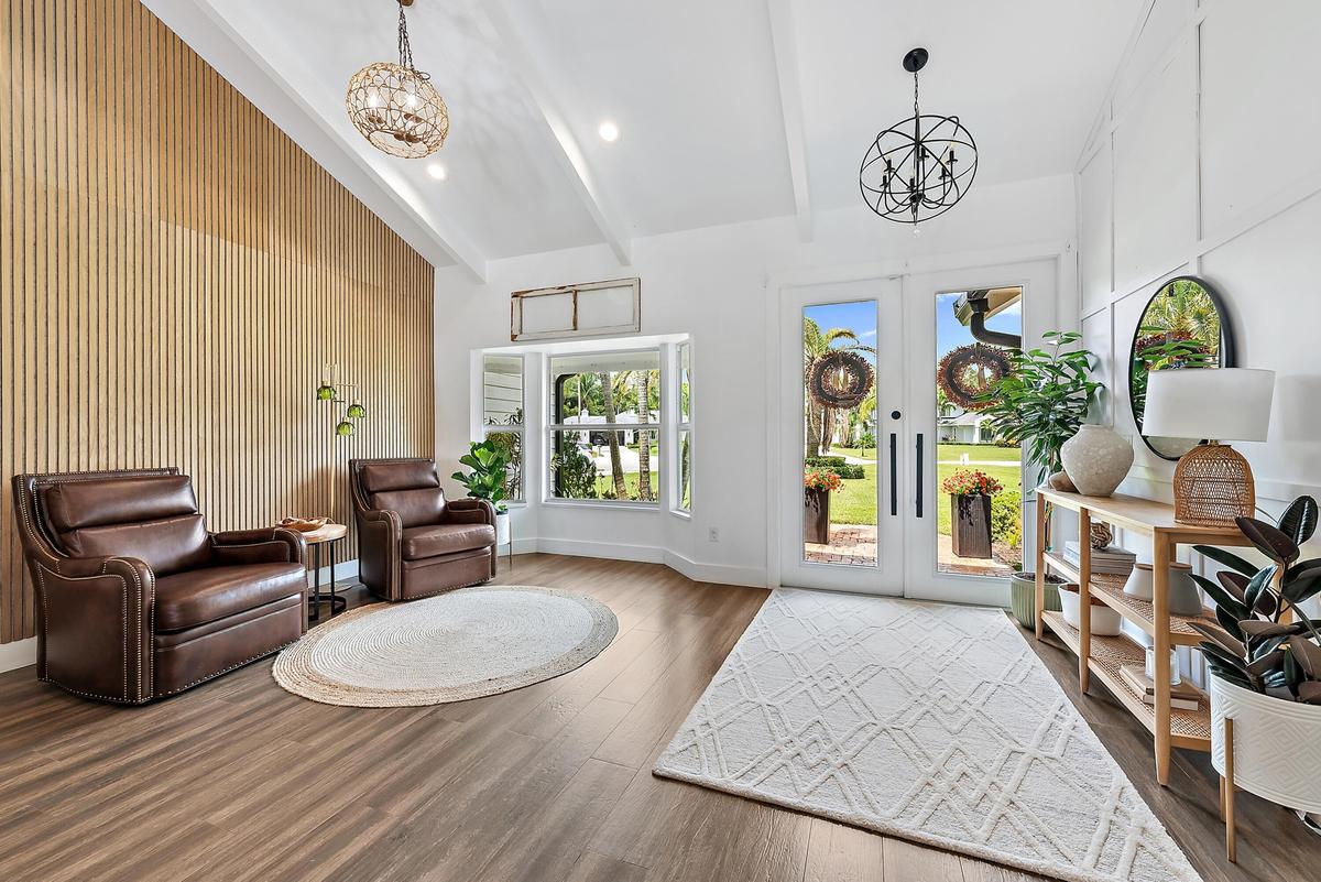 Vaulted ceiling with exposed beams, wood-look tile flooring, accent wall with vertical wood paneling, dual glass-paneled entry doors, and built-in win
