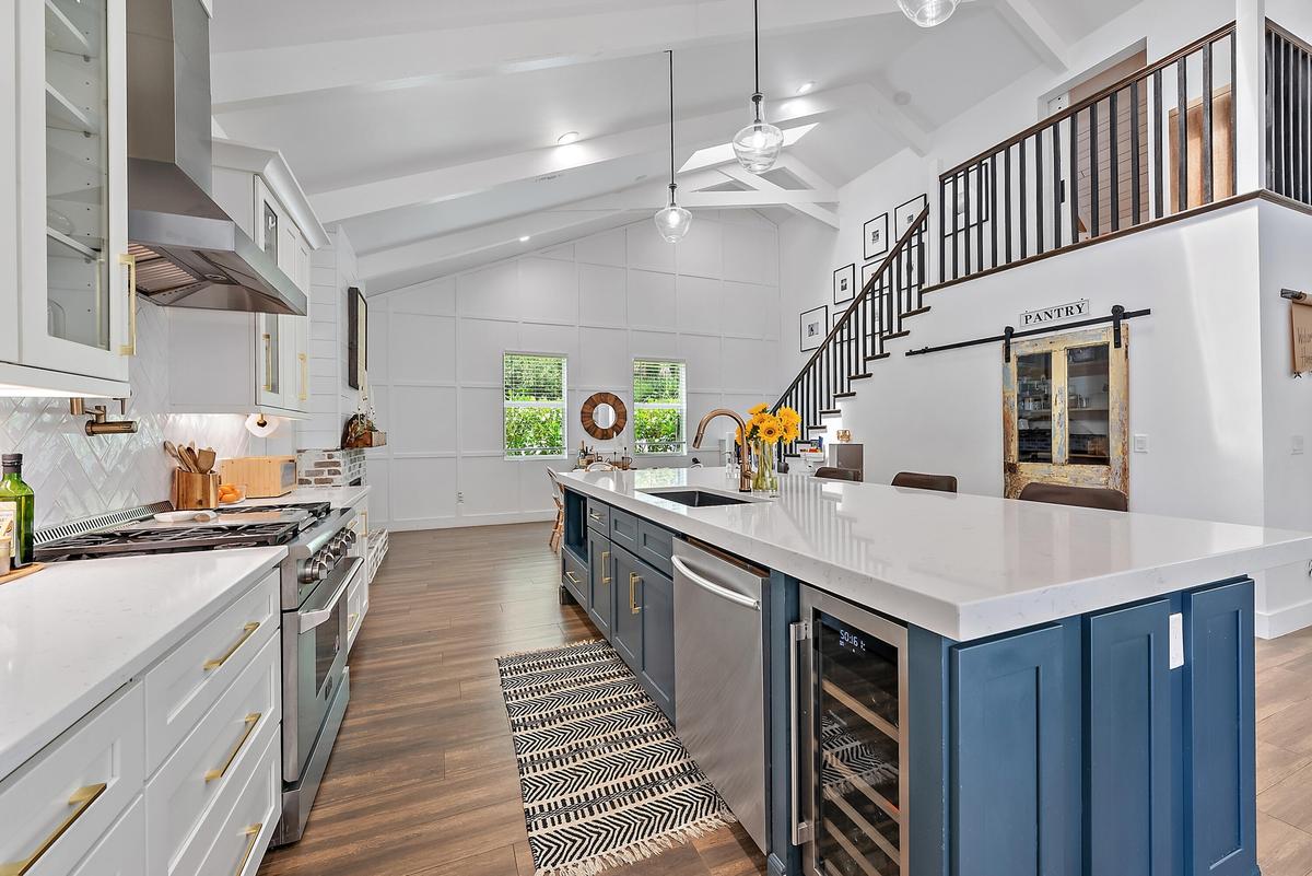 Vaulted ceilings with exposed beams, wood-finish flooring, white cabinetry with gold-tone hardware, stainless steel appliances, and a central island w