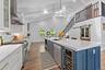 Vaulted ceilings with exposed beams, wood-finish flooring, white cabinetry with gold-tone hardware, stainless steel appliances, and a central island w