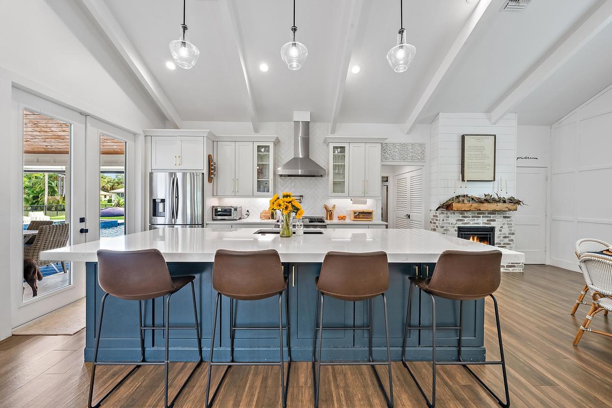 Kitchen featuring a large island with white countertop, stainless steel appliances, exposed ceiling beams, and a fireplace with a brick surround