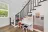 Wood-finish flooring, staircase with dark treads and white risers, white wainscoting, built-in under-stair desk, and a window with blinds