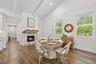 Wood-finish flooring, vaulted ceiling with exposed beams, white brick fireplace with a wood mantle, and multiple windows