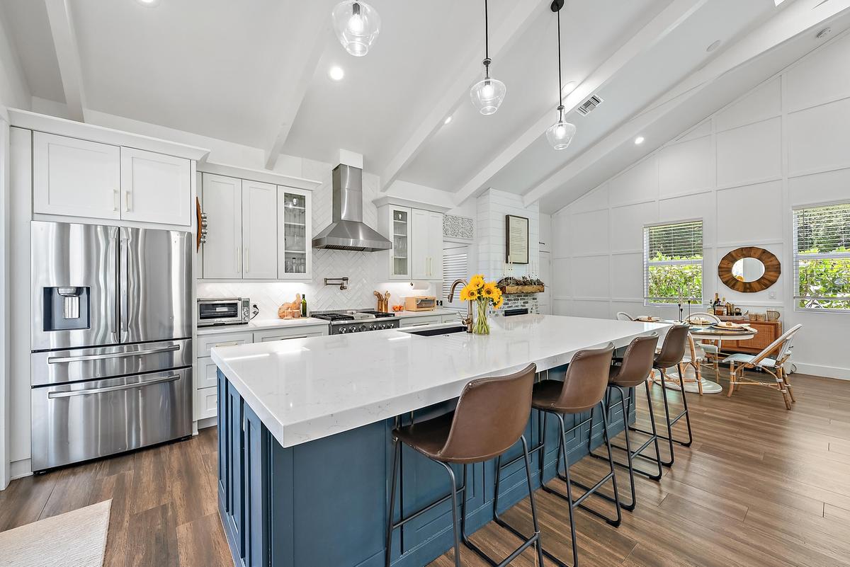 Vaulted ceiling with exposed beams, stainless steel appliances, central island with seating, pendant lighting, and wood-finish flooring