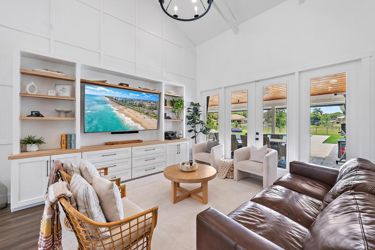 Vaulted ceiling, built-in entertainment center with wood-finish countertops, wall paneling, and multiple glass French doors leading to a covered patio
