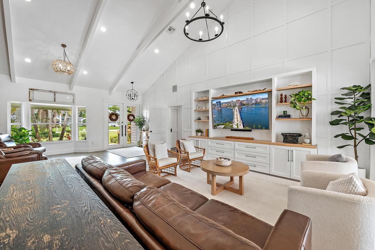 Vaulted ceiling with exposed beams, wood-look tile flooring, built-in entertainment center with open shelving, double entry doors, and large windows