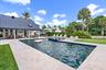 Expansive outdoor living area featuring a large swimming pool, surrounding paver patio, and lush landscaping