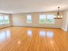 Combined living room and dining room with hardwood flooring and chandelier.
