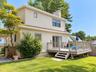 Two-story residence with shake siding, featuring a substantial outdoor deck with railing, sliding glass door access, and a wood privacy fence