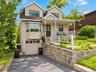 Gable roofline with dormer windows, bay window, front porch with white railings, integrated garage, and stone retaining wall
