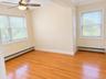 Hardwood flooring, two windows with blinds, ceiling fan, and built-in vertical cabinetry