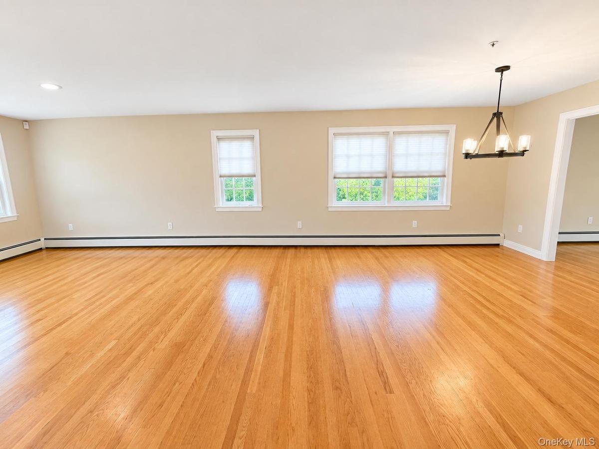 Combined Living room and dining room with hardwood flooring, multiple windows with roller shades, recessed lighting, and a dark-toned chandelier